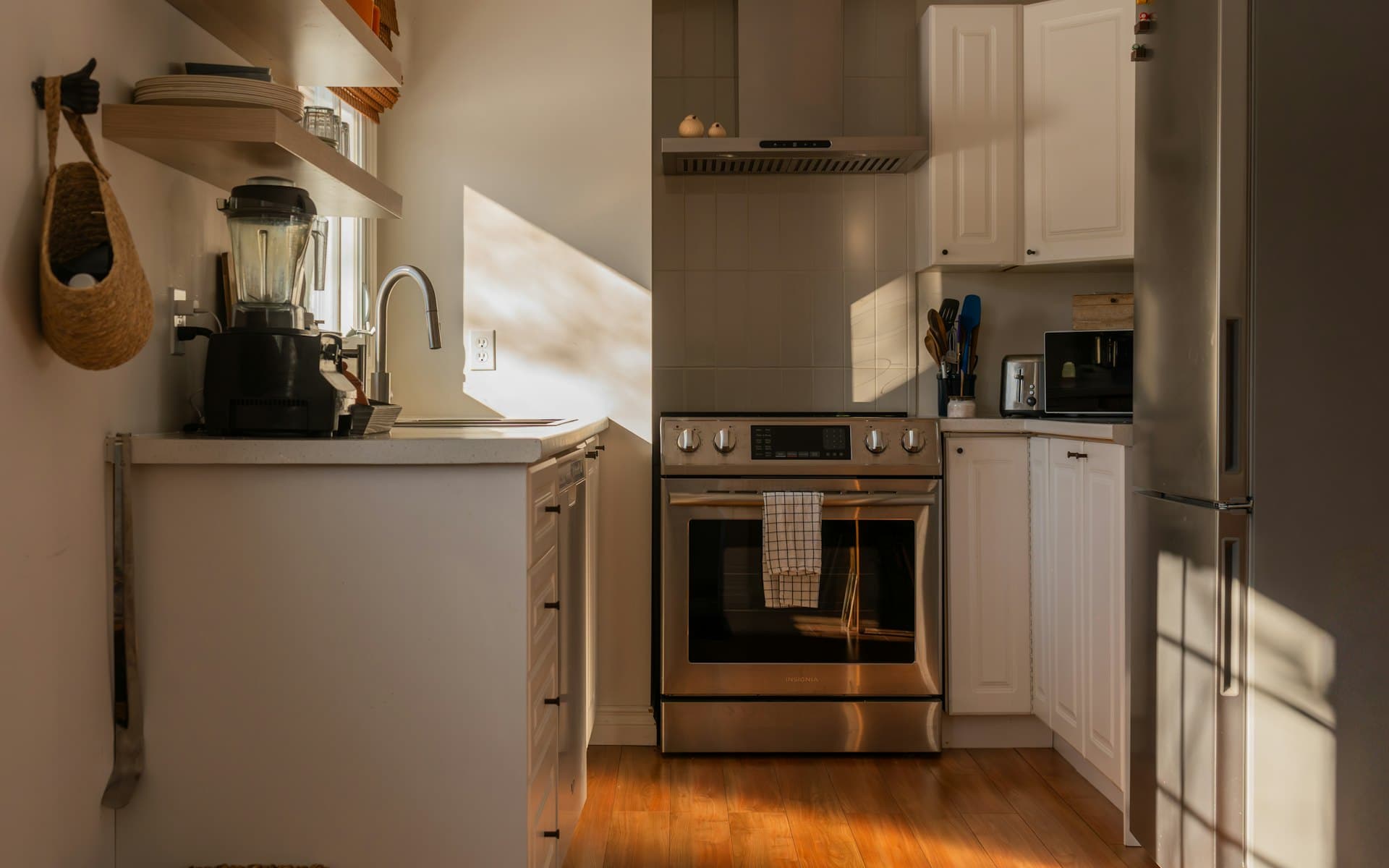 A modern kitchen with stainless steel appliances and wooden floors in morning light.