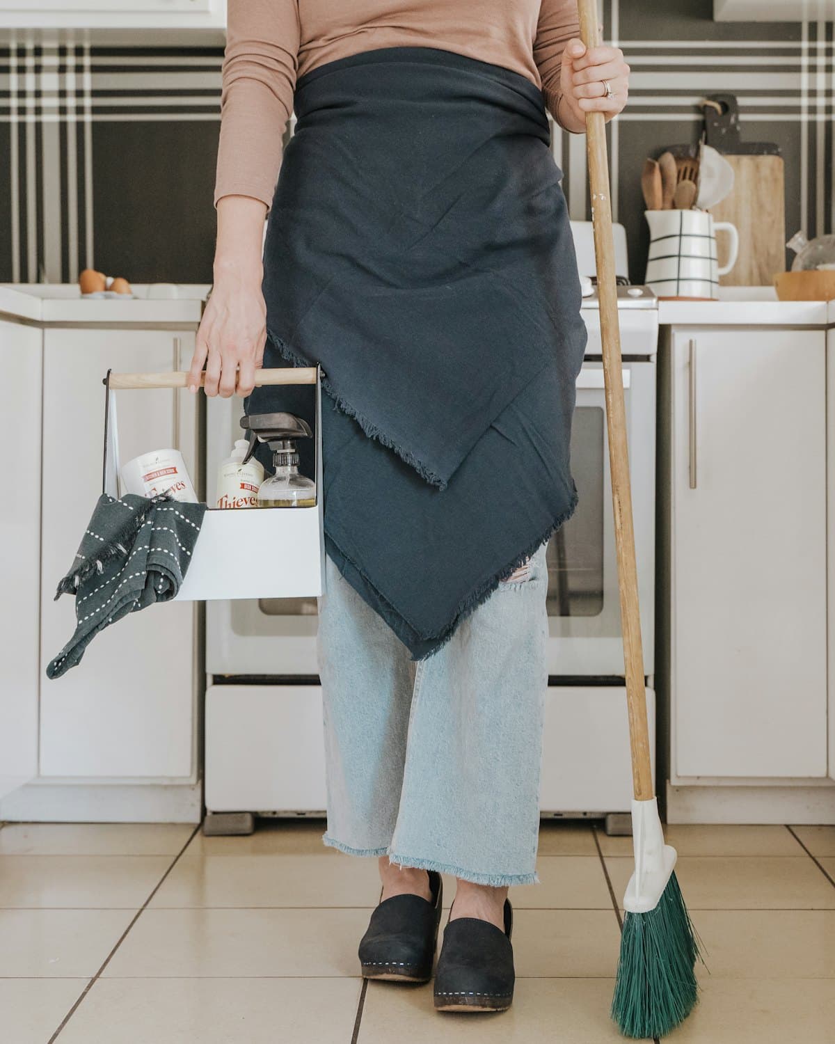 A cleaner standing in a residential kitchen holding a broom.