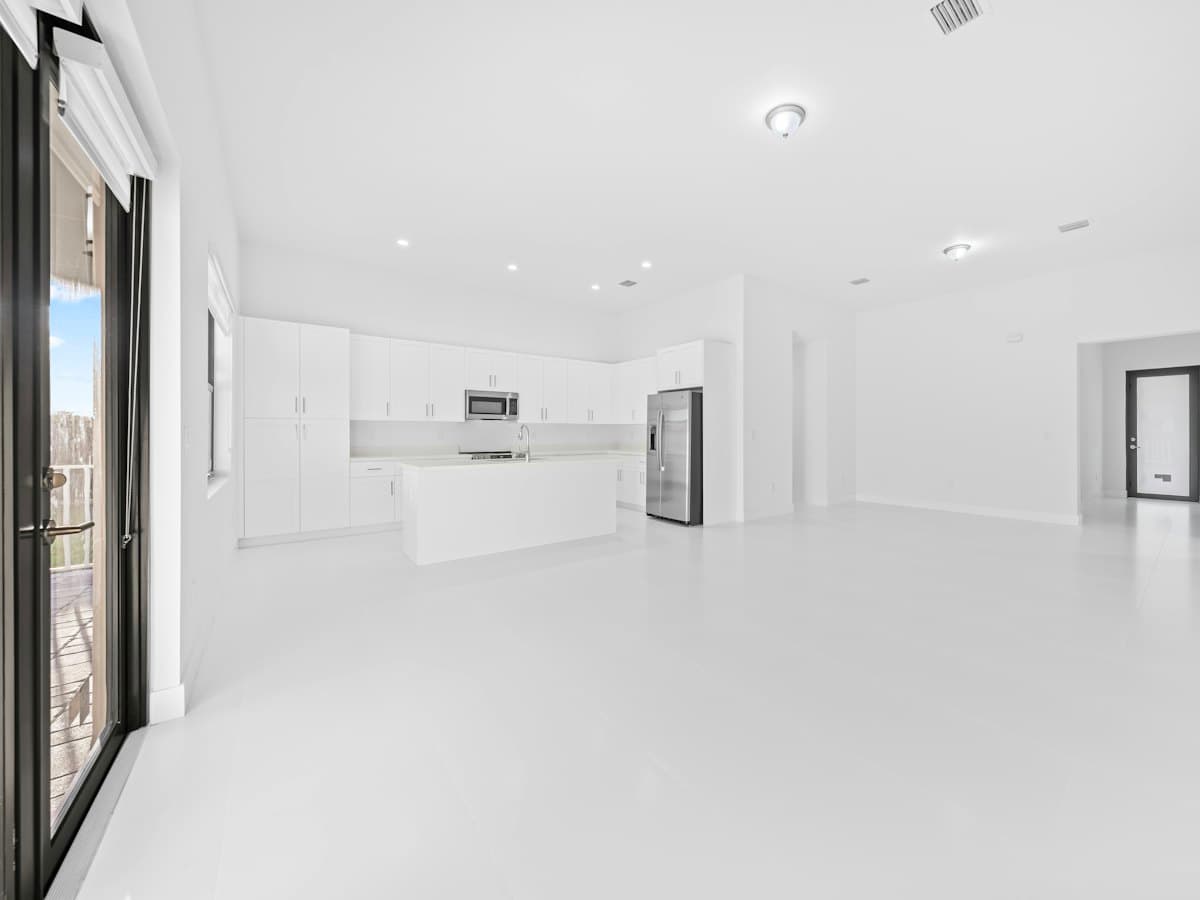 An empty modern white kitchen and living area with large windows.