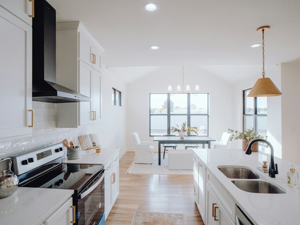 A clean kitchen with a sink, stove and a window letting in daylight.